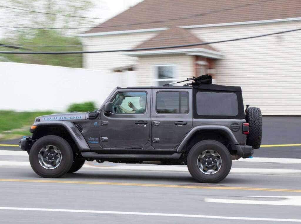 a gray jeep driving down a street next to a house